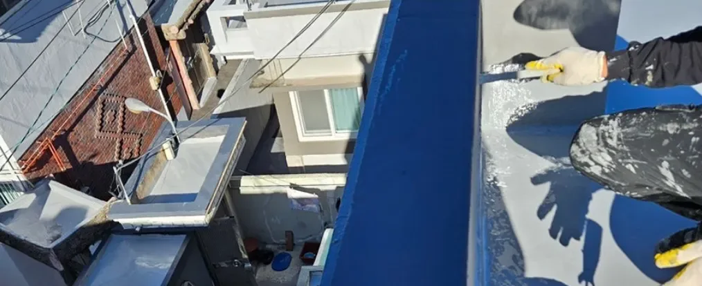 옥상 난간 안쪽에 파란 도막을 바르는 작업 장면